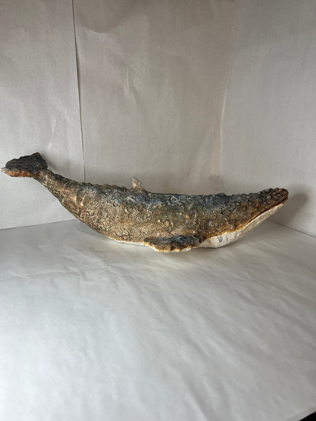Keramikskulptur af pukkelhval set fra siden med halefluksen hævet, mørk blåbrun og hvid
