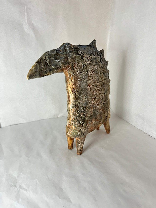 Keramikskulptur af fabeldyr set skråt fra siden, viser de fire spidse ben og ru mineralgrå overflade
