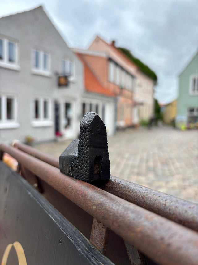 Hus #13 fra Harritsø foran et brolagt torv - tårn med bobletekstur i næsten sort bronze