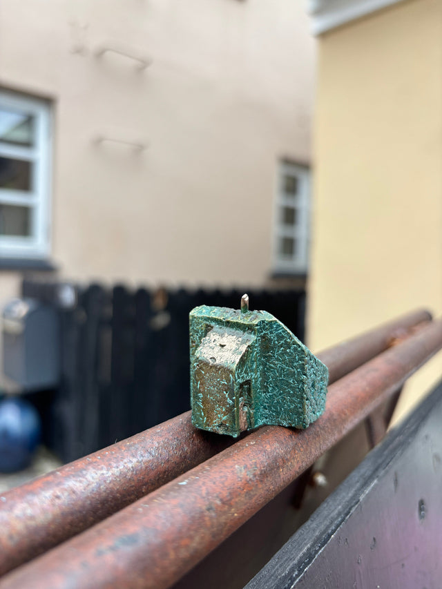 Hus #19 fra Harritsø på en rusten gelænder - blågrøn bronze skulptur med asymmetrisk tagform