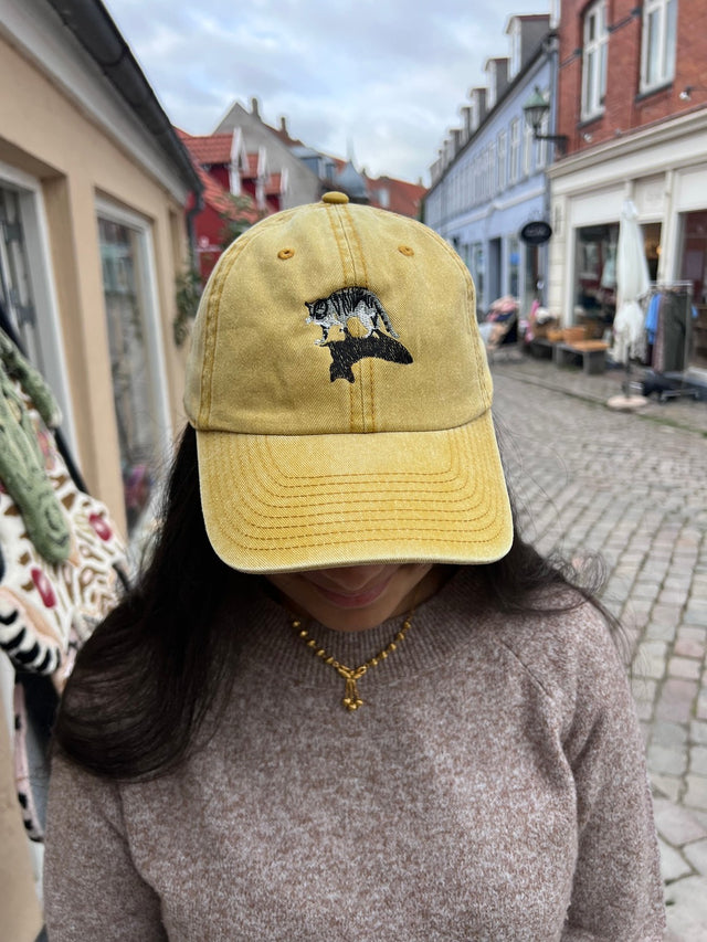 Kasket med broderet kat med skygge i karry gul fra Rustfelt, fotograferet i Ebeltofts gågade