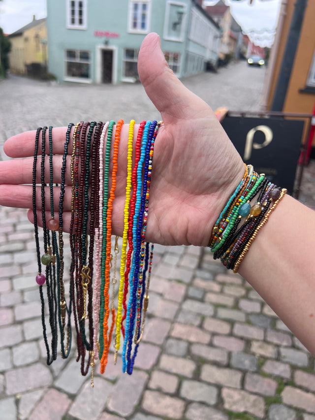 Hånd med vifte af farverige Annavii glasperlearmbånd foran brolagt gade i Ebeltoft