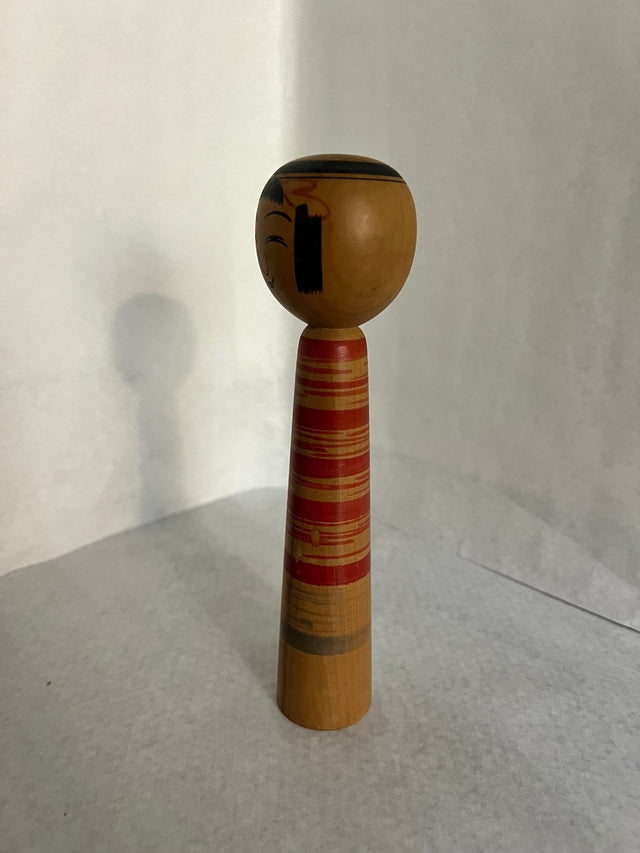 Vintage kokeshi #22 set fra siden. Røde striber øverst og naturligt træ. 19 cm