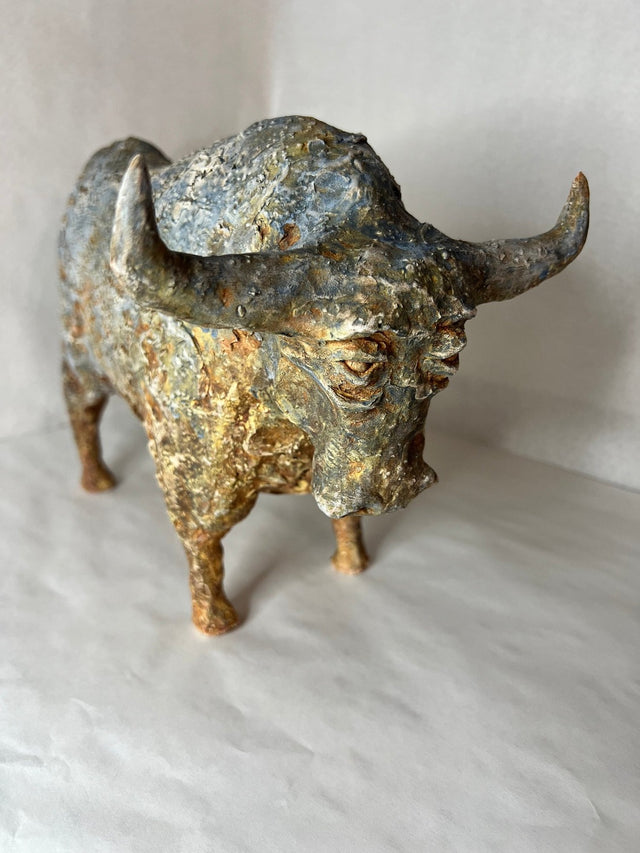 Keramikskulptur af bison set forfra med sænket hoved og brede horn i blågrå og gyldne toner